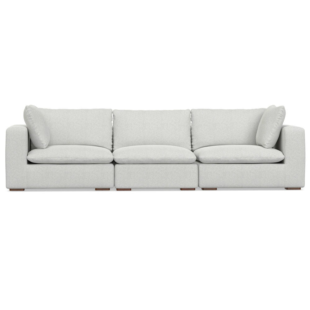 The Jasmine - Handcrafted Sofa is a modern, light gray three-seater featuring plush back and side cushions, wide armrests, and low wooden legs, shown against a white background.