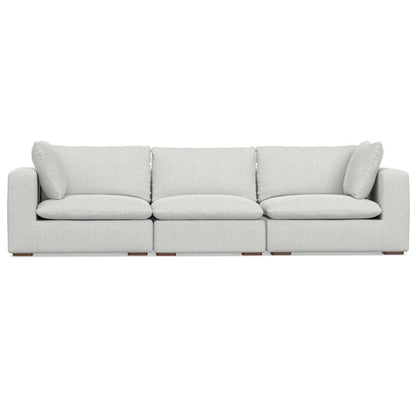 The Jasmine - Handcrafted Sofa is a modern, light gray three-seater featuring plush back and side cushions, wide armrests, and low wooden legs, shown against a white background.