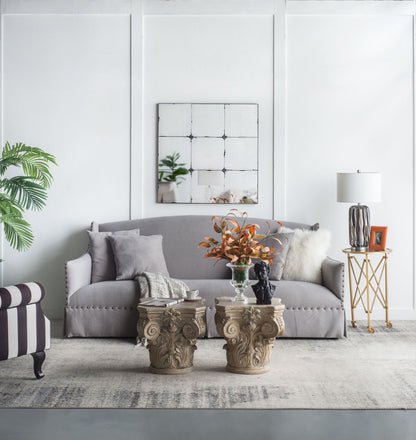 A modern living room with a gray sofa, neutral pillows, stone pedestal coffee tables, a plant, striped chair, gold side table with lamp and photo, and a Traditional Decor Style Antique Glass Panel Mirror above the sofa.