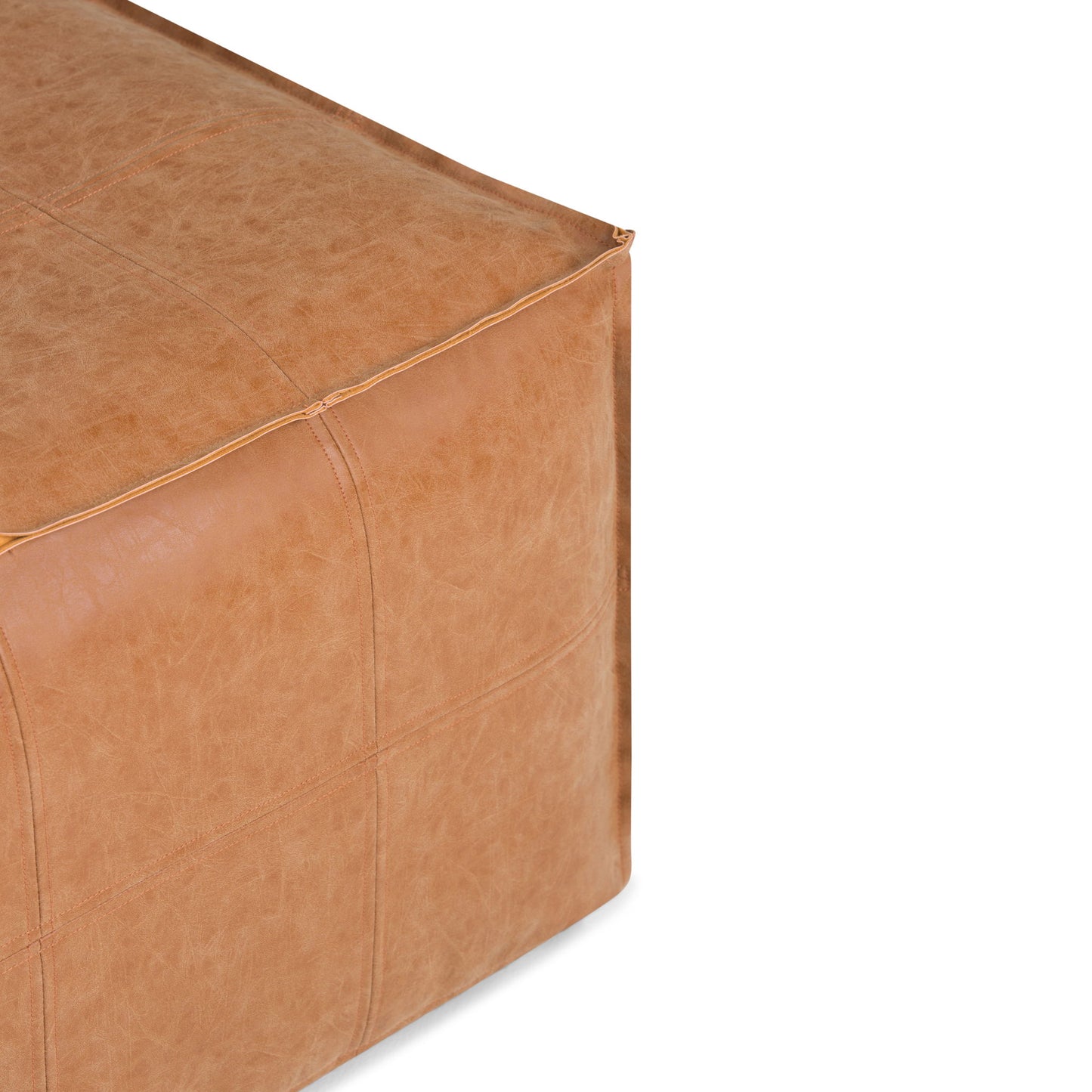 Close-up of the Brody Large Square Coffee Table Pouf in tan leather, showing detailed stitching and a soft, textured surface. Only a portion of the pouf is visible against a white background.