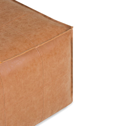 Close-up of the Brody Large Square Coffee Table Pouf in tan leather, showing detailed stitching and a soft, textured surface. Only a portion of the pouf is visible against a white background.