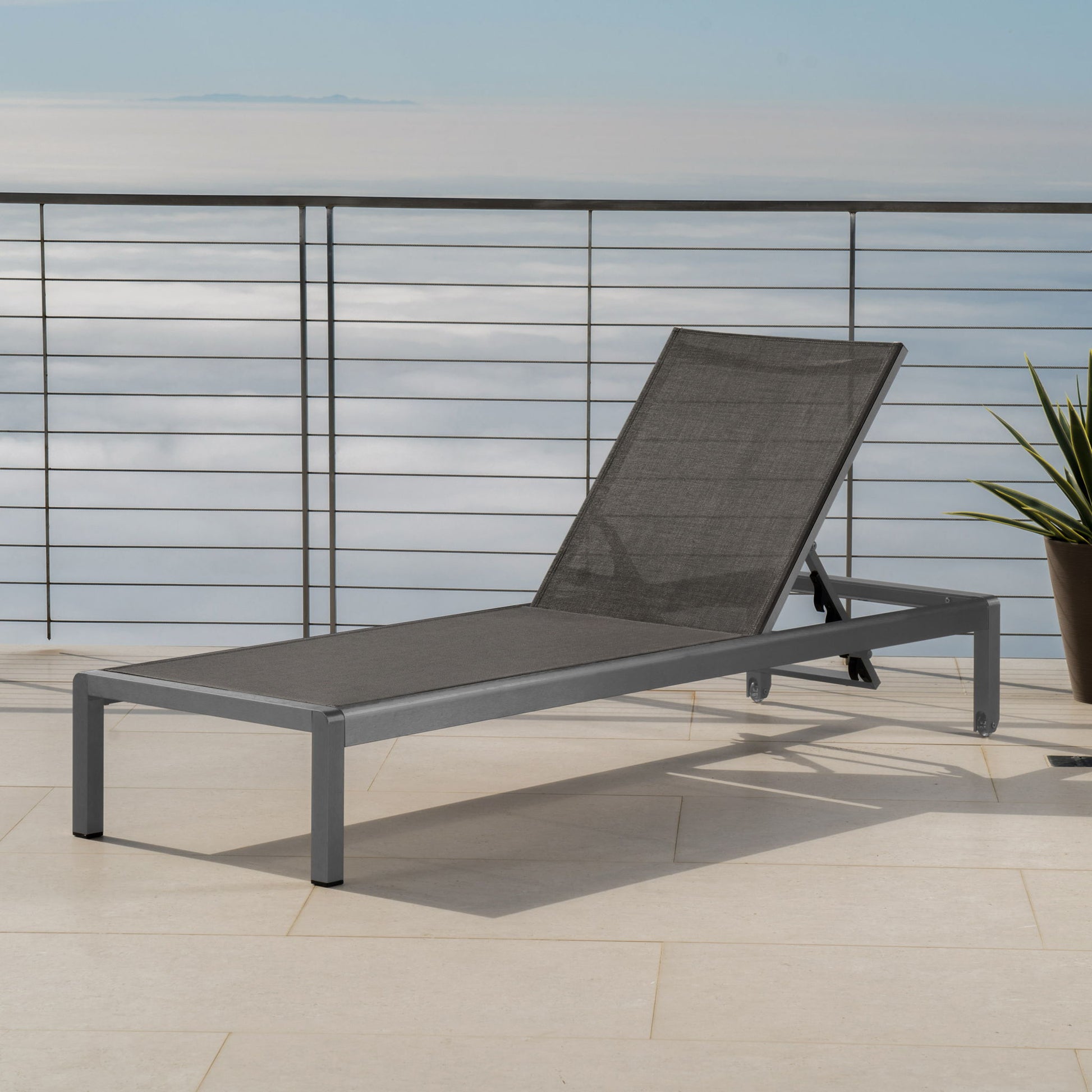 The Outdoor Patio Chaise Lounge with 5 Reclining Positions, featuring a mesh seat and backrest, is placed on a tiled patio with metal railing and potted plant, overlooking clouds and blue sky.