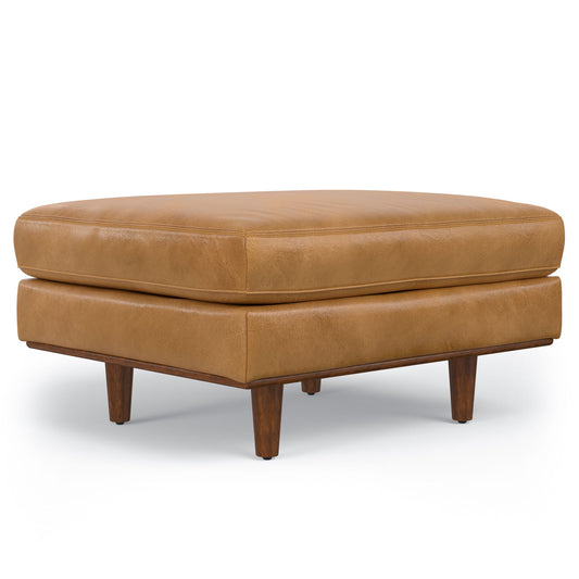 The Morrison - Handcrafted Ottoman features a square shape, light brown leather upholstery, a cushioned top, and sturdy wooden legs, shown against a white background.