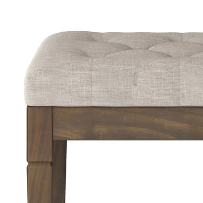 A close-up of the Waverly Upholstered Tufted Ottoman Bench shows its light beige tufted cushion and a wooden frame with a dark brown finish.