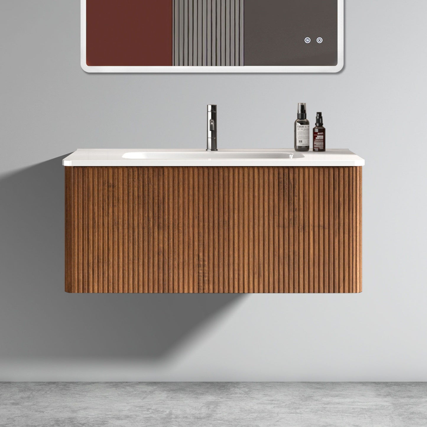 The Etna Striped Bathroom Vanity features a ribbed wooden cabinet, ceramic sink, and chrome faucet. Two bottles sit on the right of the white countertop. Minimalist decor with a gray wall and concrete floor completes the modern look.