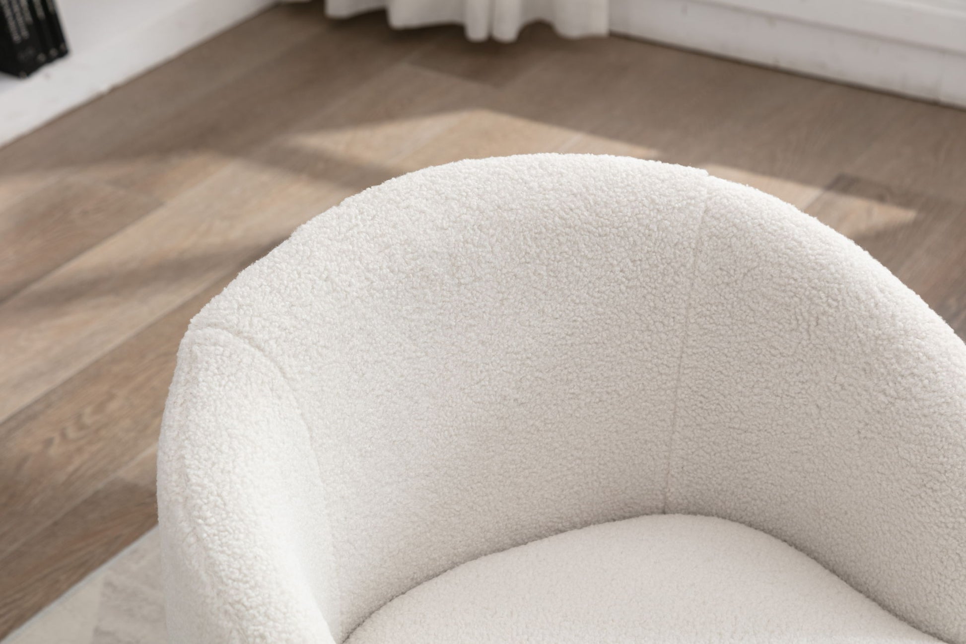 A close-up view of the Teddy Fabric Swivel Accent Armchair Barrel Chair with a powder coating metal ring on a wooden floor, illuminated by natural light through a window with white curtains in the background.