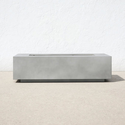 The Modern Concrete Design Propane Outdoor Fire Pit Table, featuring a minimalist rectangular shape, rests on a light beige surface with a plain white textured wall behind it. The design is sleek, with no visible flames or extra decorations.