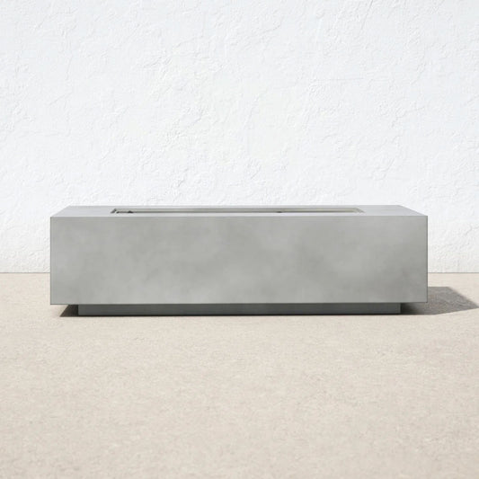 The Modern Concrete Design Propane Outdoor Fire Pit Table, featuring a minimalist rectangular shape, rests on a light beige surface with a plain white textured wall behind it. The design is sleek, with no visible flames or extra decorations.