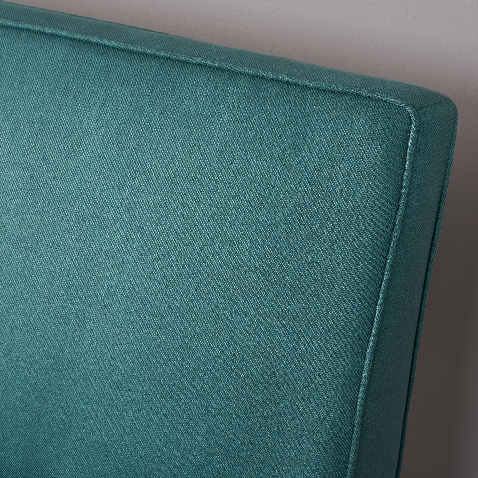 Close-up of the upper corner of the Contemporary Loveseat With Upholstered Fabric And Birch Wood Legs in teal, set against a light gray wall.