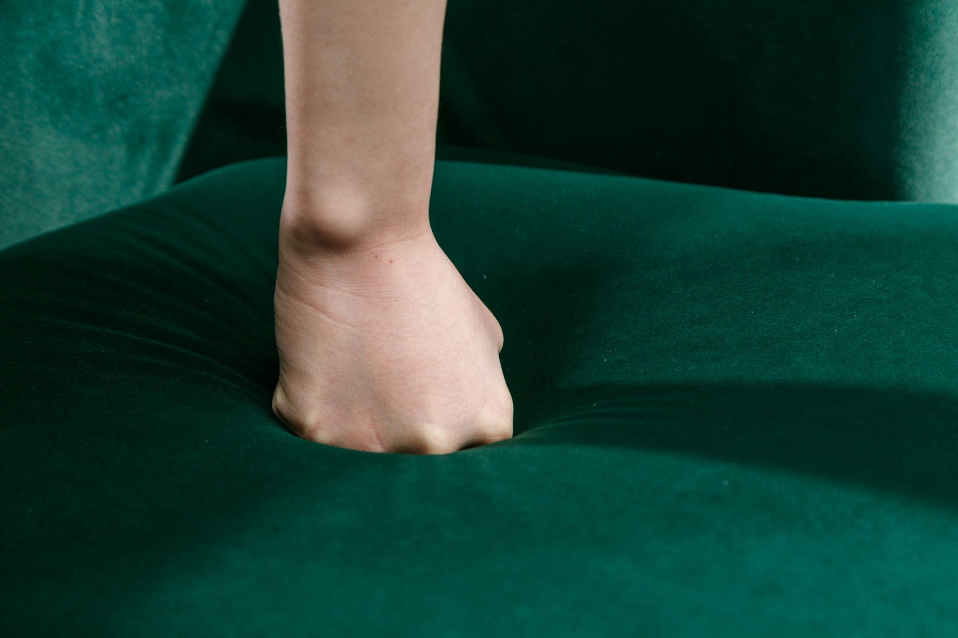 A close-up of a person's clenched fist pressing into the soft green velvet of the Barrel Chair, creating a deep indentation in the plush fabric of this Swivel Accent Armchair with Powder Coating Metal Ring.