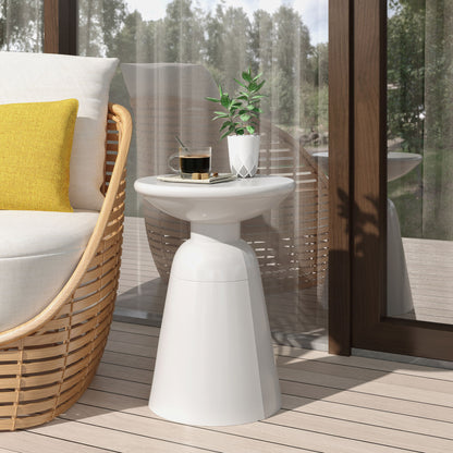 A modern patio features a wicker chair with a yellow cushion and an Outdoor Modern Metal End Large Table holding a coffee cup, saucer, spoon, and potted plant. Glass doors and trees can be seen in the background.