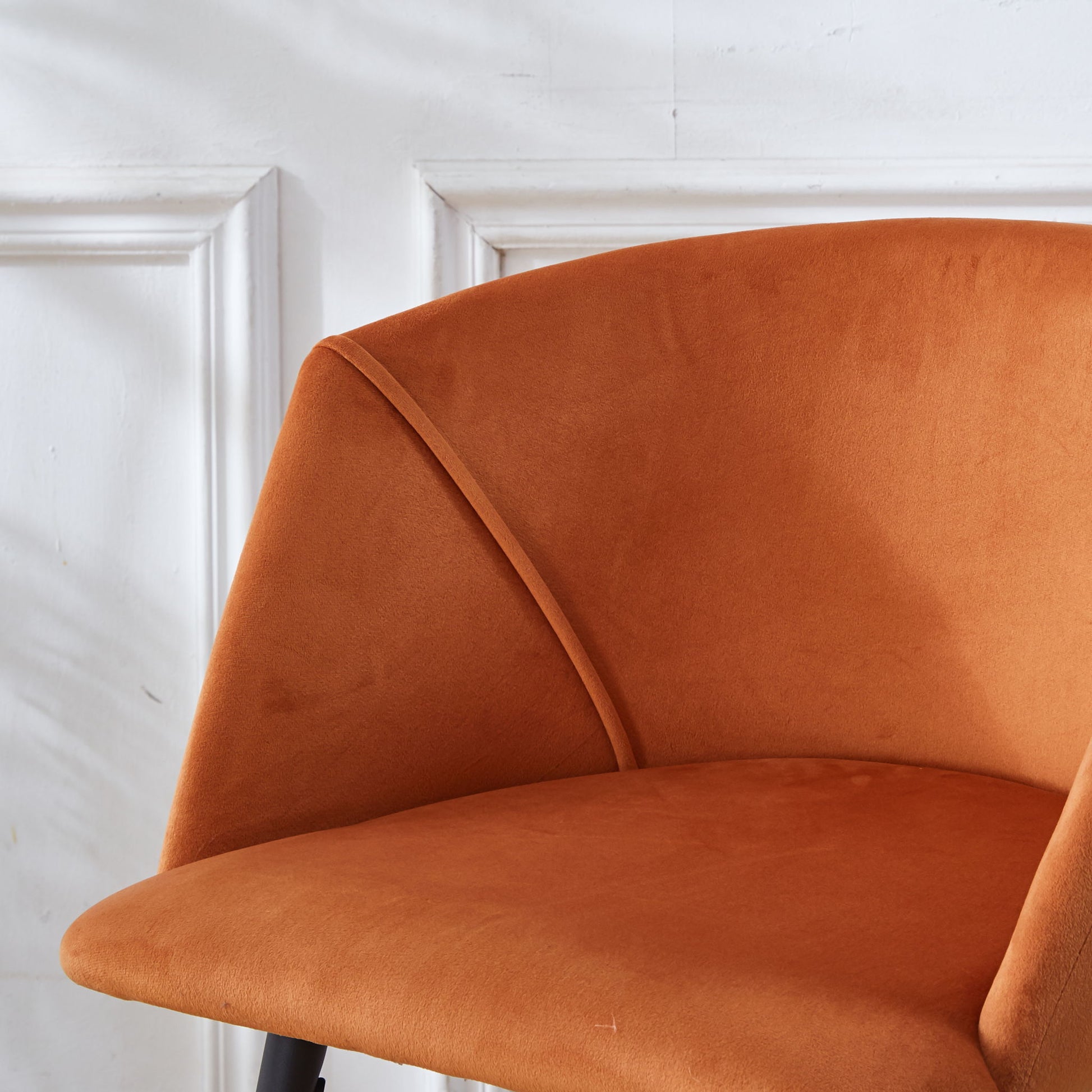 A close-up of a Counter Height Bar Stool with metal legs (set of 2), featuring orange velvet upholstery and a curved backrest, showcased in front of a white wall with decorative molding.