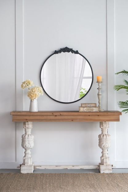 A rustic console table holds a vase of white flowers, books, and a candle. Above it hangs the Classic Design Mirror with Baroque Inspired Frame, leaning against a white paneled wall.