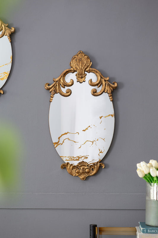 The Decorative Oval Wall Mirror, Accent Mirror for Living Room, Entryway, or Bedroom with gold trim and marble-like accents hangs on a gray wall. At the bottom right corner are a vase of white tulips and stacked books.