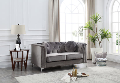 A bright living room features the Stylish Sloped Arm Loveseat in gray with round pillows, a tall potted plant, a lamp and books on a side table, cups on a tray atop a light rug, set before large arched windows with curtains.