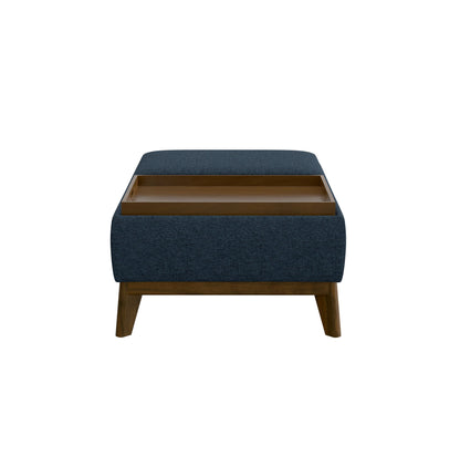 The Varia Reversible Tray Ottoman in blue features wooden legs, a cushioned top with partially open storage beneath, and is shown against a plain white background.