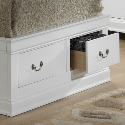 The Louis Phillipe Bookcase Storage Bed features a white wooden drawer unit at its base with silver handles. One drawer is open, revealing dark bedding inside. The bed sits on a wood floor beside a patterned rug.
