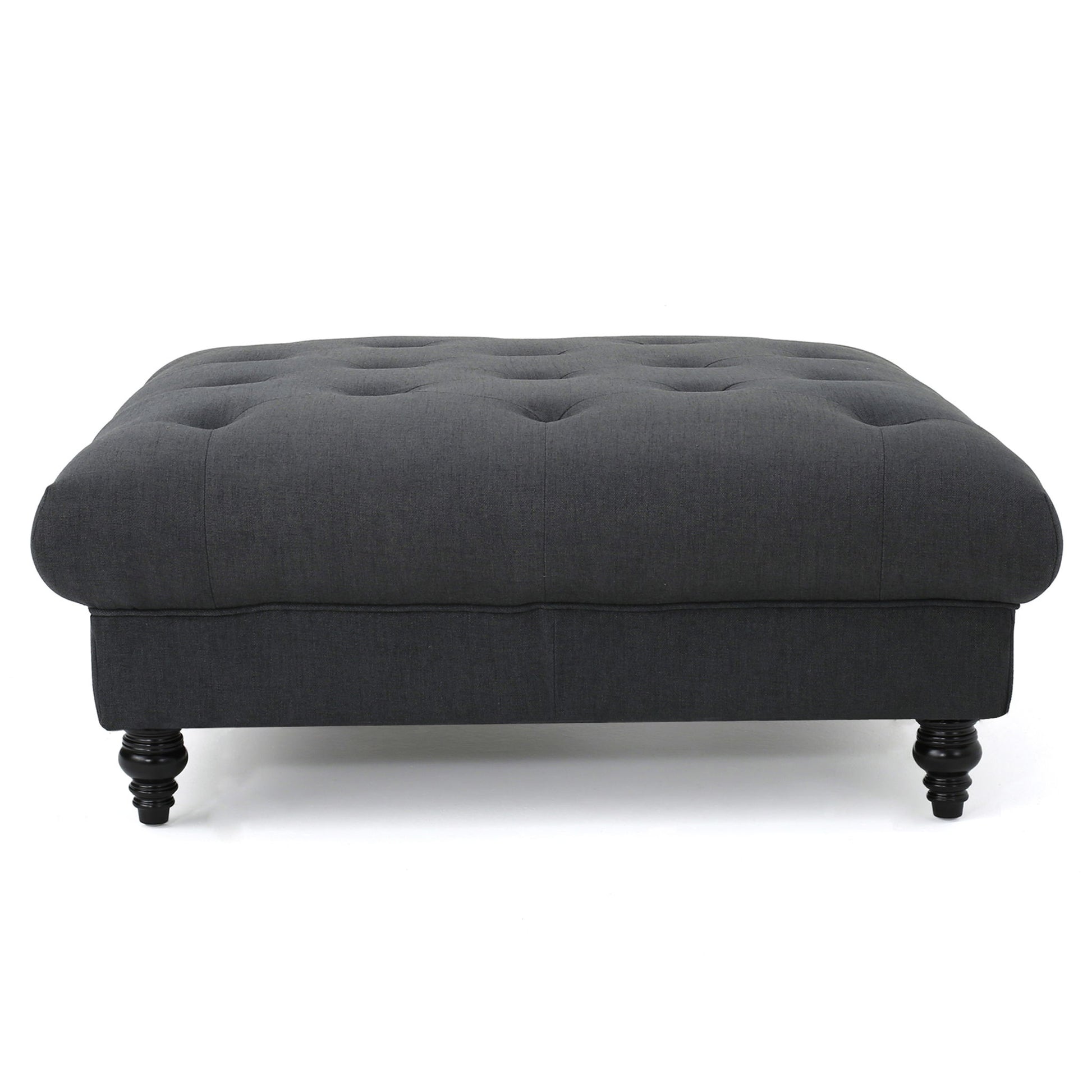 The Madrid - Tufted Ottoman Footrest is a dark gray, rectangular piece with a tufted top and four short, turned wooden legs, displayed against a white background.
