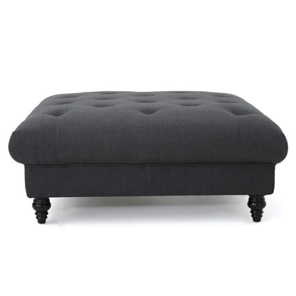 The Madrid - Tufted Ottoman Footrest is a dark gray, rectangular piece with a tufted top and four short, turned wooden legs, displayed against a white background.