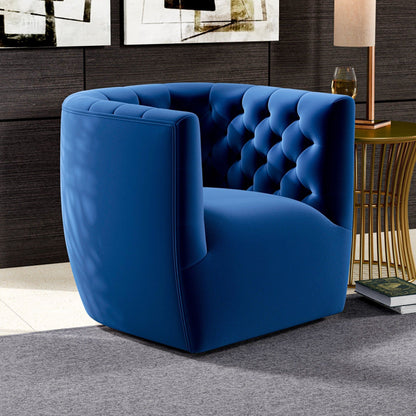 The Delaney Ergonomic Design Swivel Chair in blue velvet with a tufted backrest sits on a gray rug next to a gold side table with a lamp and glass, set in a chic room featuring dark wood walls and abstract art.