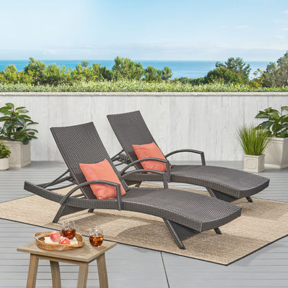 Two Salem - Contemporary Wicker Chaise Lounges with coral cushions sit on a patio rug facing lush greenery and an ocean view. A nearby wooden table holds drinks and apples, surrounded by potted plants.