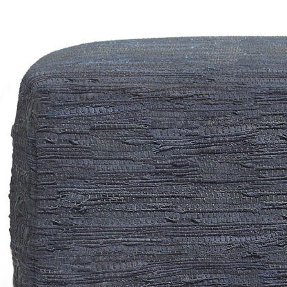 Close-up of Fredrik - Handcrafted Square Pouf in dark blue textured fabric with uneven horizontal stitches, tightly wrapped around its edge. The background is plain white.