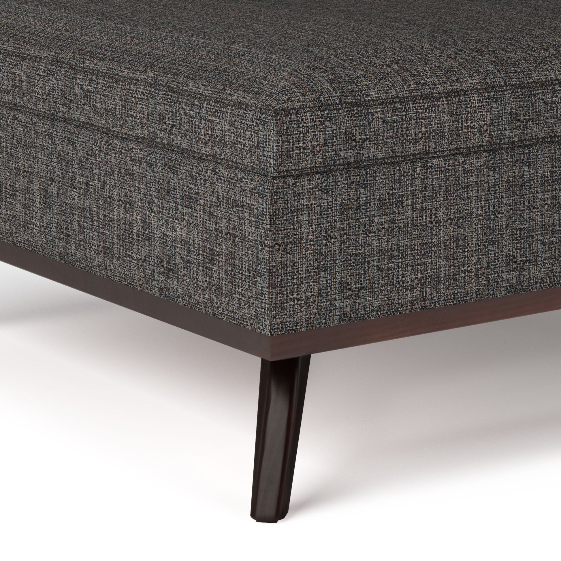 Close-up of the corner of the Owen - Multifunctional Square Coffee Table Storage Ottoman in dark gray upholstery with a subtle textured fabric and wooden legs, shown against a white background.