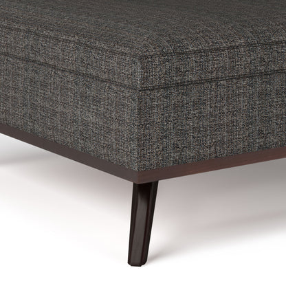 Close-up of the corner of the Owen - Multifunctional Square Coffee Table Storage Ottoman in dark gray upholstery with a subtle textured fabric and wooden legs, shown against a white background.