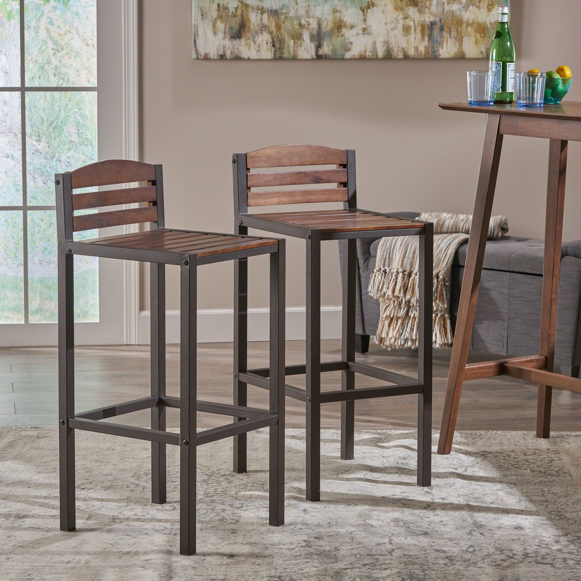 A set of two Outdoor Barstools With Slat Panel Design in dark brown stand on a light rug in a modern living space, placed by a wooden table with drinks and near a sofa with a beige throw.