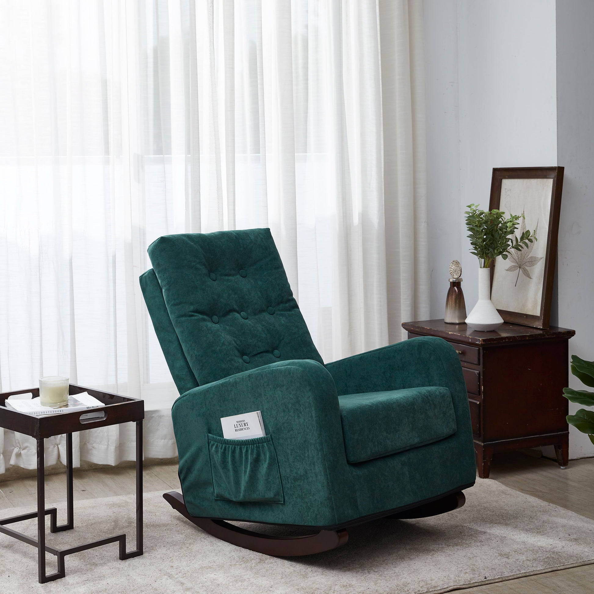 A Single Sofa Reclining Japanese Chair, upholstered in green, with a side pocket, is placed near a window with sheer curtains in a bright living room. Nearby are a small table holding a candle and a wooden cabinet decorated with ornaments.