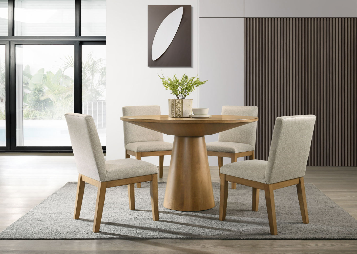 A modern dining room features the Jasper Wide Contemporary Round Dining Table with four fabric chairs, set atop a gray rug. A vase with greenery decorates the table, while large windows and minimalist wall art complete the space.