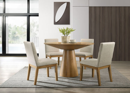 A modern dining room features the Jasper Wide Contemporary Round Dining Table with four fabric chairs, set atop a gray rug. A vase with greenery decorates the table, while large windows and minimalist wall art complete the space.