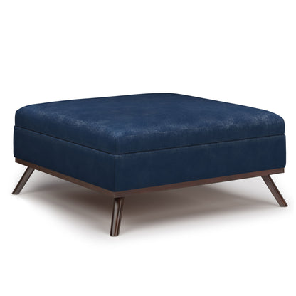 The Owen Multifunctional Square Coffee Table Storage Ottoman features dark blue upholstery, angled wooden legs, and a simple, minimalist design for modern style and added storage.