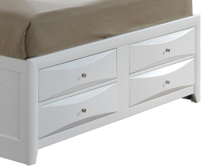 A close-up of the Marilla Storage Bed With Bookcase Headboard, featuring a white wooden frame with four drawers, each with a silver knob. A beige sheet is partially visible on the mattress above the drawers.