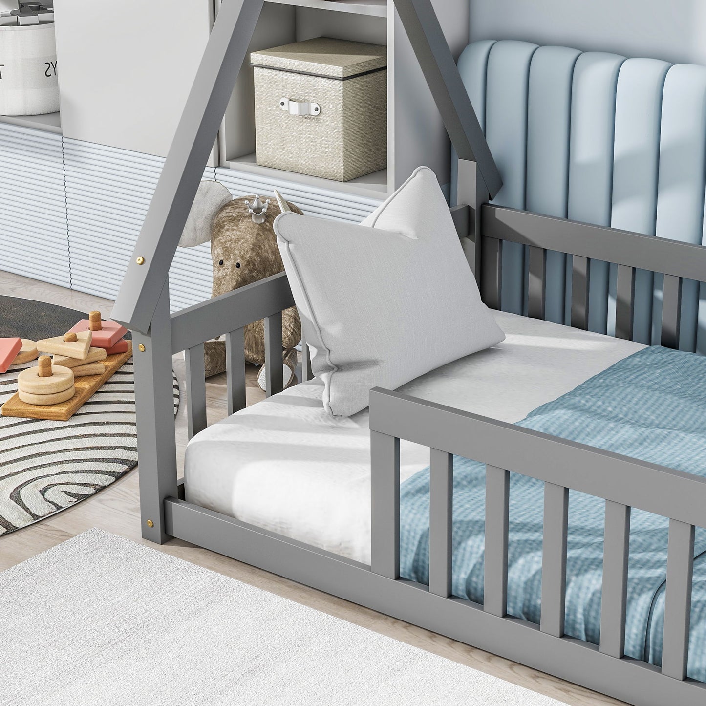 A modern gray Tent-Shaped Floor Bed, Teepee Bed with guardrails and slats, features a house frame design, light blue padded headboard, white bedding, blue blanket, and pillow. Toys, a plush animal, and storage baskets complete the bright room.