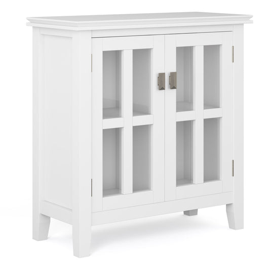 The Artisan - Handcrafted Low Storage Cabinet features a white wood finish, two glass-paneled doors with silver handles, an interior shelf, four short legs, and a simple modern design.