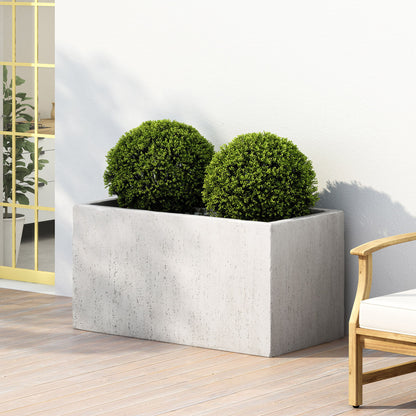 The Modern Outdoor Planter, a rectangular concrete design, holds two round green bushes and sits on a wooden deck beside a white-cushioned wooden chair near a yellow-trimmed glass door.