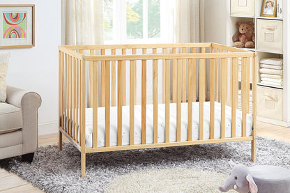 The Palmer - 3-in-1 Convertible Island Crib with a white mattress stands on a gray rug in a bright nursery. Nearby shelves hold folded linens and a teddy bear, while a plush gray elephant toy rests on the floor.