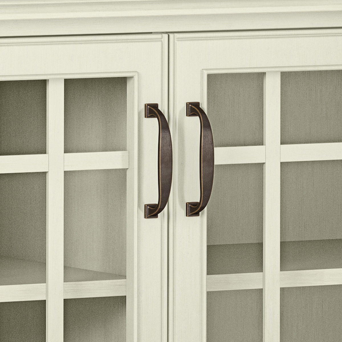Close-up of two bronze handles on the white-framed glass doors of the Connaught - Handcrafted Low Storage Cabinet, with interior shelves visible through the glass panels.