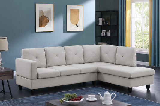 A modern living room with blue walls, abstract art, a floor lamp, a window with yellow curtains, a coffee table set with fruit and a teapot, and the Santiago - Linen Sectional Sofa With Right Facing Chaise in light gray.