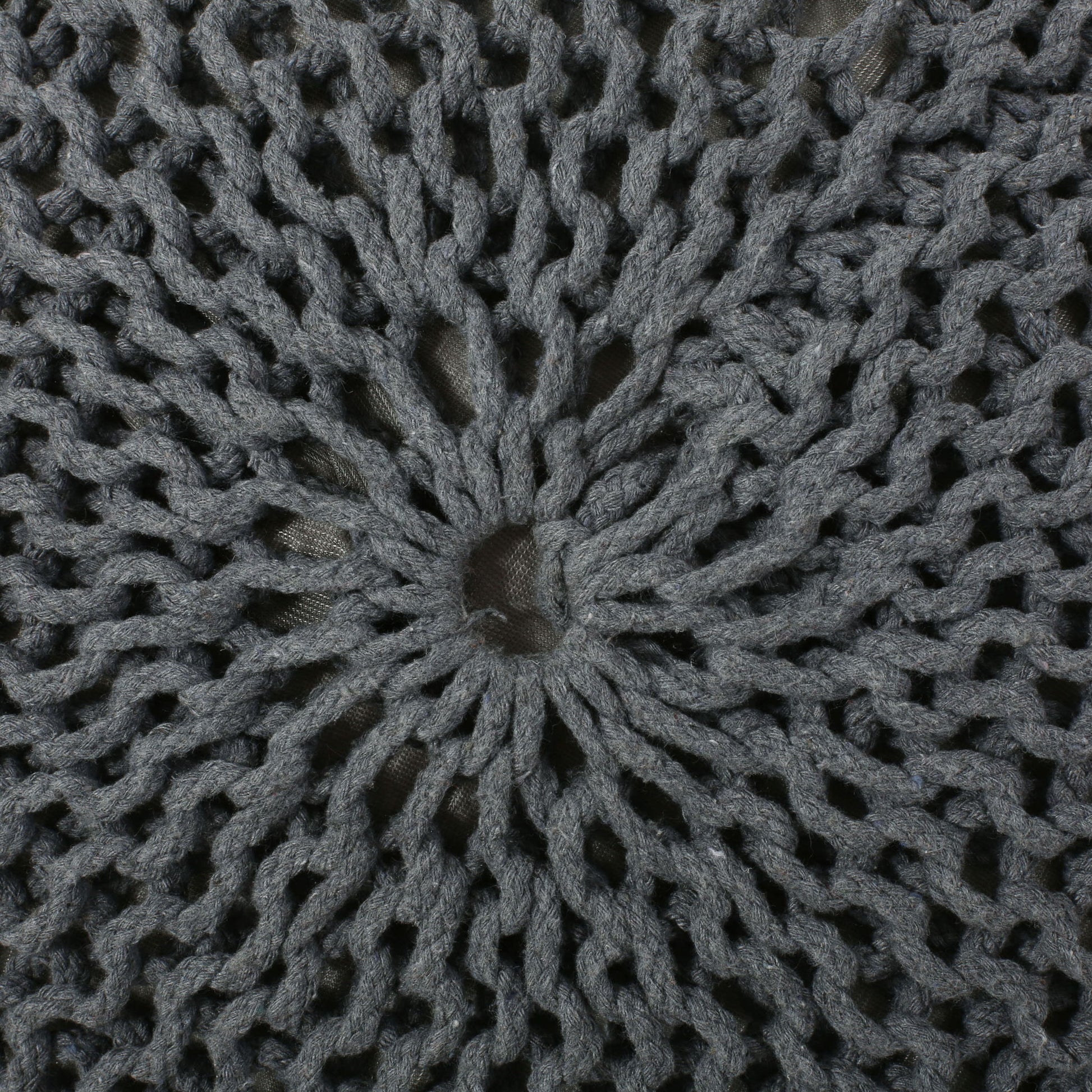 Close-up of the Bordeaux Knitted Cotton Round Pouf shows its gray, open-knit sunburst design with a center hole, allowing the background fabric to show through. This versatile ottoman also works as a stylish floor cushion.
