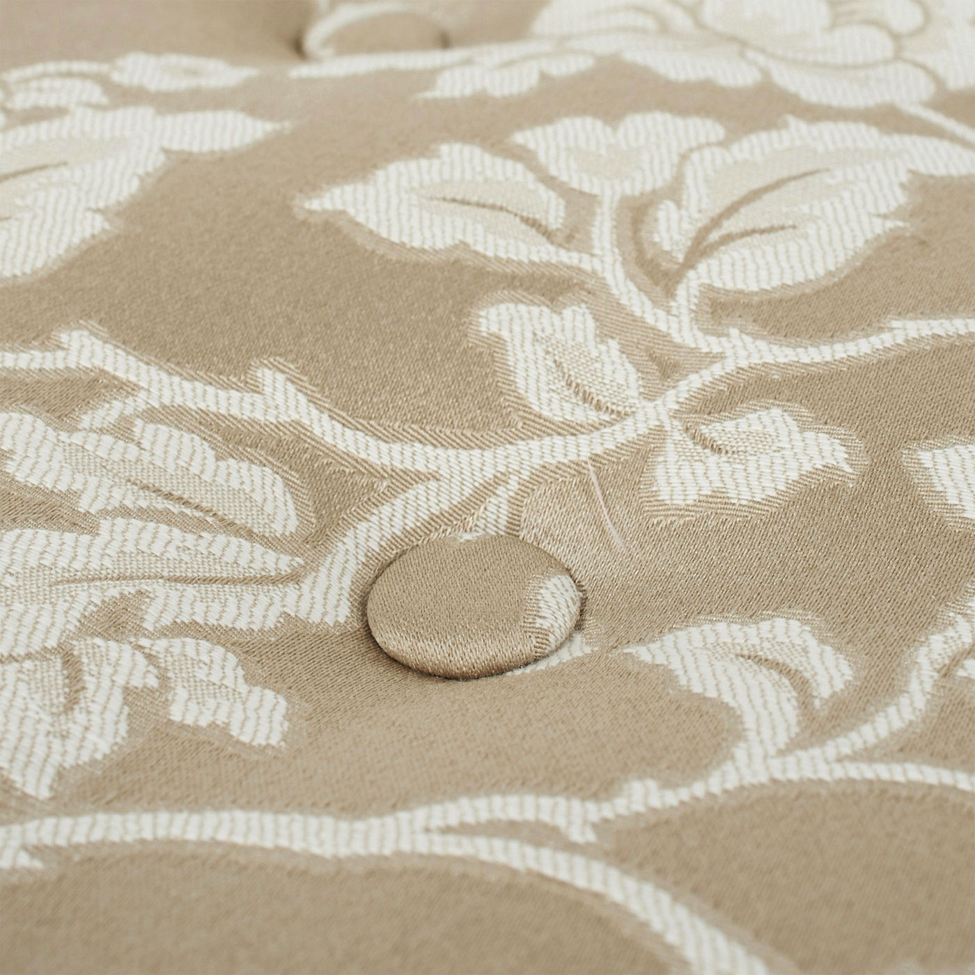 Close-up of the Yolanda Round Upholstered Accent Ottoman featuring a beige fabric with a white floral pattern and a centered, fabric-covered button tuft showcasing its detailed texture and design.