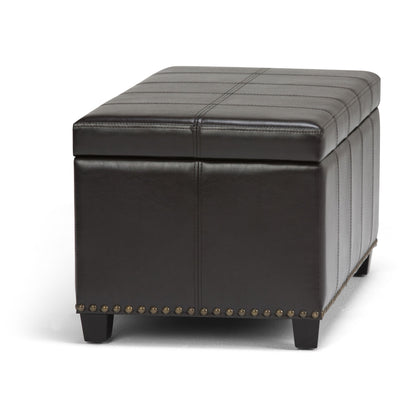 The Amelia Transitional Storage Ottoman Bench features a rectangular dark brown leather design with decorative stitching, metal stud accents along the bottom edge, and short wooden legs.