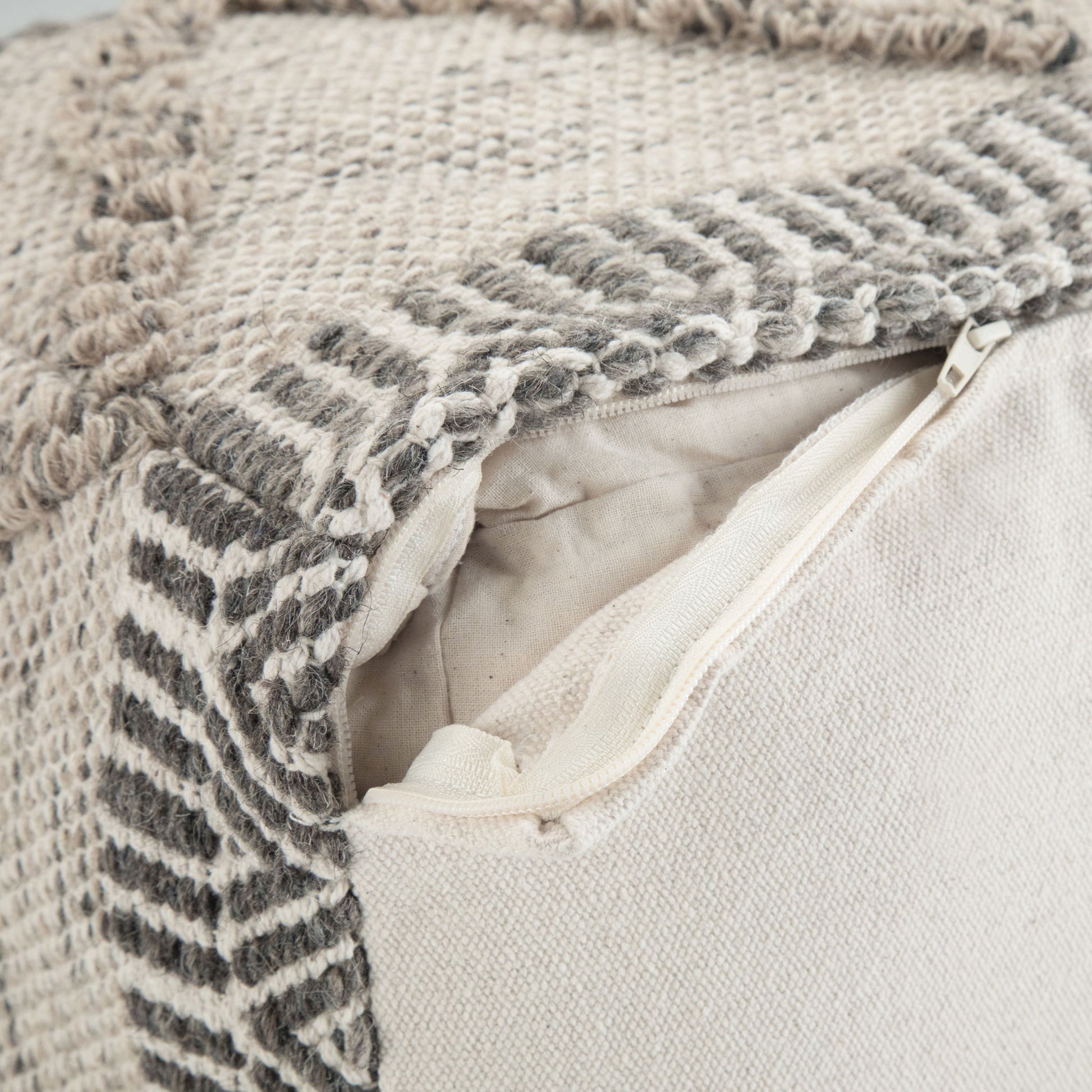Close-up of the Sweeney Upholstered Square Pouf featuring a textured, geometric woven pattern in beige and gray, with an open zipper displaying the inner pillow.