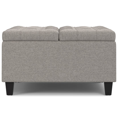The Harrison Upholstered Coffee Table Storage Ottoman features a rectangular gray tufted top and short black legs, displayed from the front on a white background.