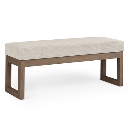 The Milltown Upholstered Ottoman Bench features a rectangular beige upholstered seat and simple open wooden legs, displayed against a white background.