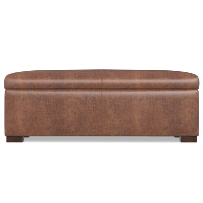 The Gabbie Coffee Table Upholstered Storage Ottoman is rectangular, brown leather with a smooth cushioned top and short dark wooden legs, shown from the front.