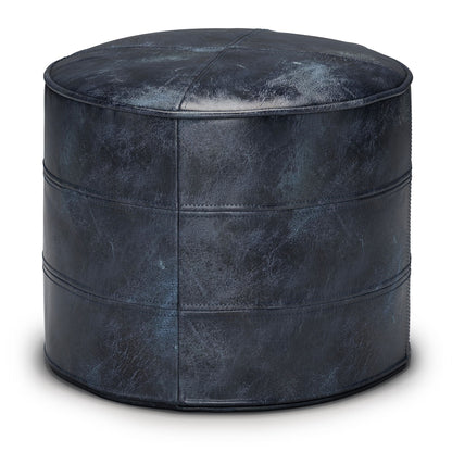 The Connor - Handcrafted Round Pouf is a dark blue leather ottoman with visible stitching and a slightly distressed finish, displayed against a white background.