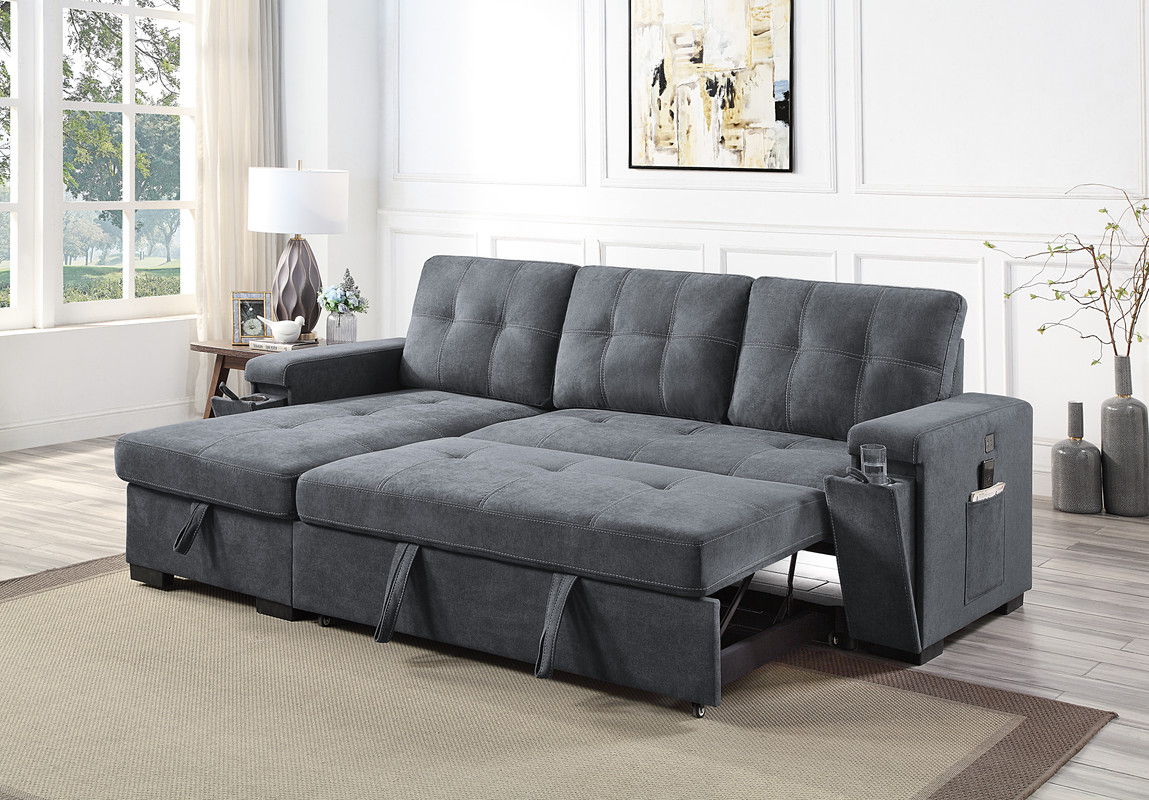 A modern living room with the Toby Woven Fabric Reversible Sleeper Sectional Sofa featuring storage chaise, cup holders, charging ports, and pockets, set on a beige rug near a window with light curtains and a potted plant.