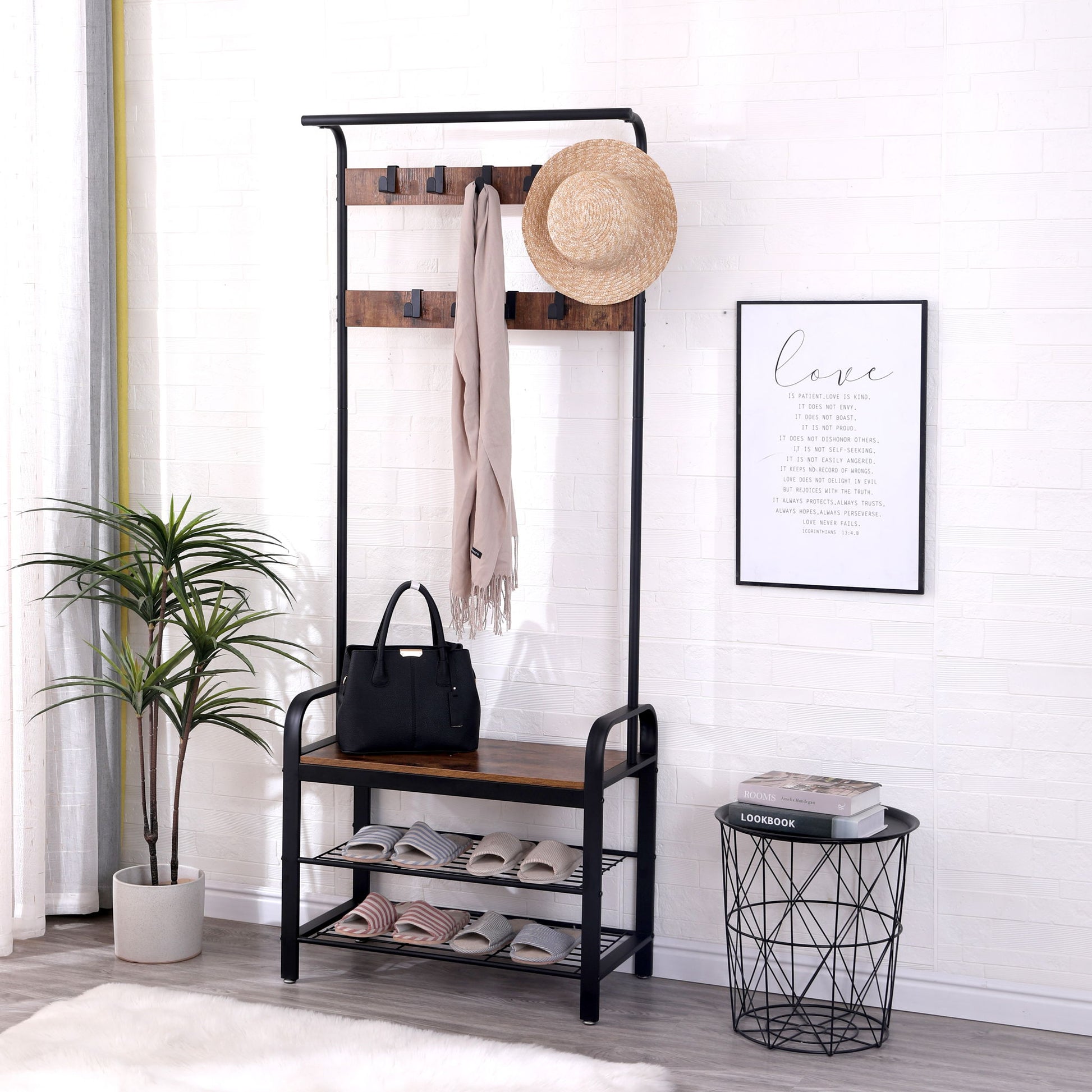 A stylish entryway features the Hall Tree With Shoe Bench For Entryway With 9 Removable Hooks, displaying a hat, scarf, black handbag, and shoes. A framed quote hangs on a white brick wall beside a wire table with books and a potted plant.